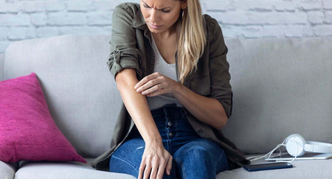 Uncomfortable young woman scratching her arm while sitting on the sofa at home.